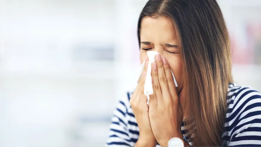 Image of a young woman with allergies sneezing into a tissue.