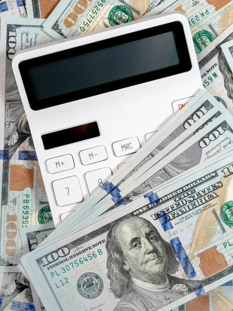 A calculator with a blank screen is placed on top of a scattered array of United States currency notes.