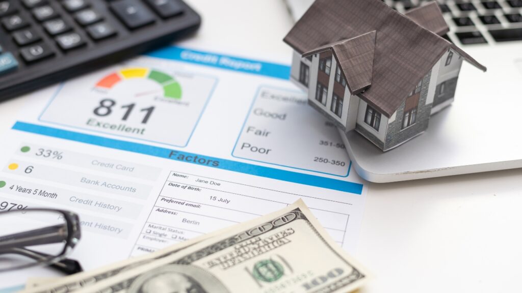 A credit report showing a score of 811 labeled "Excellent," with a small model house on top of the document, a calculator, and cash in the background.