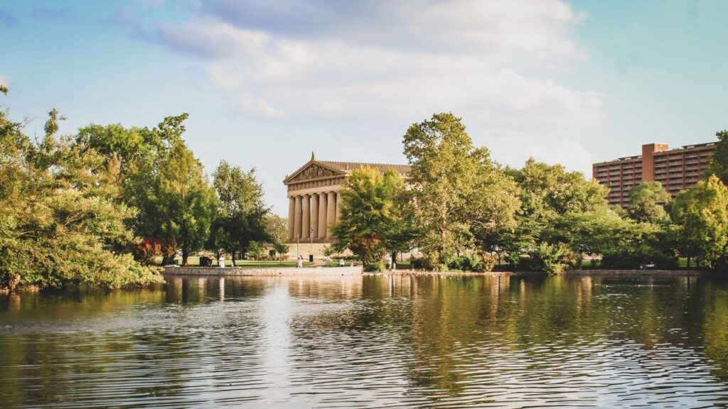A view of the Parthenon replica in Nashville behind a lake surrounded by trees.