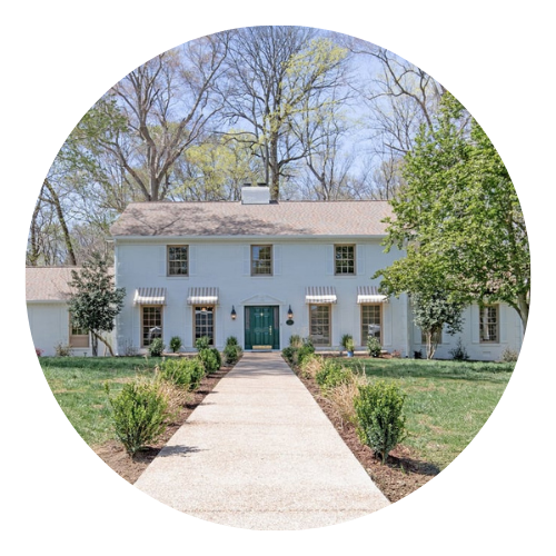 White two-story house with a green front door, striped awnings, and a straight walkway.