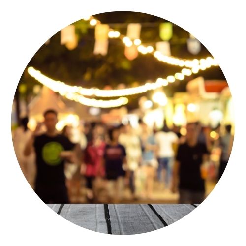 Blurry crowd at a lively outdoor night market with string lights.