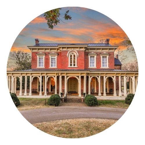 Historic red-brick mansion with white columns at sunset.
