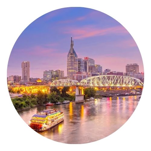 Nashville skyline at sunset with a riverboat cruising under a lit bridge.