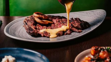 Grilled steak topped with crispy onion rings and drizzled with a creamy yellow sauce.