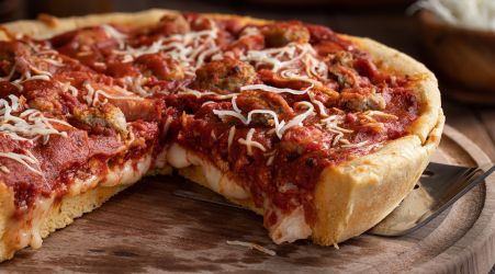 A deep-dish pizza topped with meatballs, marinara sauce, and shredded cheese on a wooden tray.
