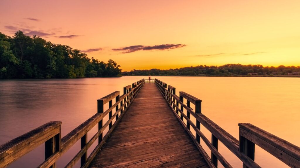 A wooden pier stretching over a lake during a golden sunset.