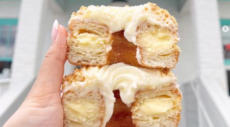 A hand holding two stacked cream-filled croissant donuts topped with frosting.