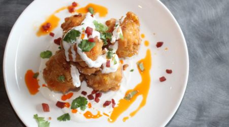 Crispy fried bites topped with a creamy sauce, herbs, and orange drizzle on a white plate.