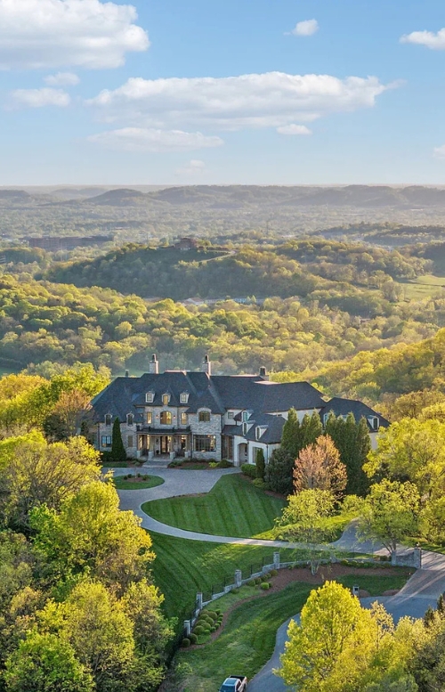 Large estate home with a slate roof surrounded by trees on a hilltop with scenic valley views in the background.
