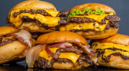 A stack of cheeseburgers with bacon and lettuce on toasted buns.