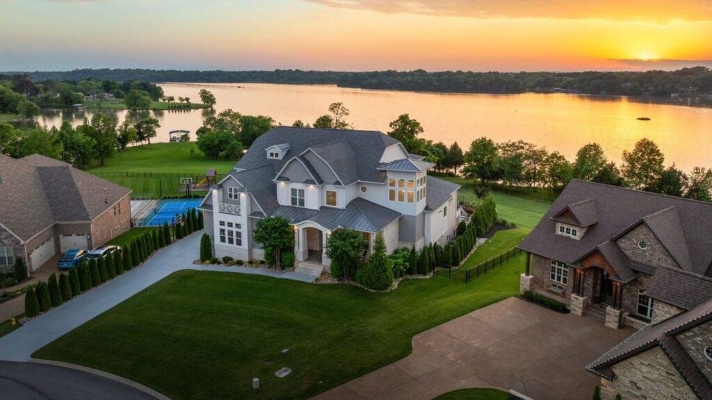 A large waterfront house overlooking a peaceful lake at sunset.