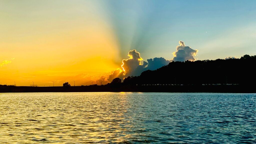 A dramatic sunset over a lake with clouds lit by the sun's rays.