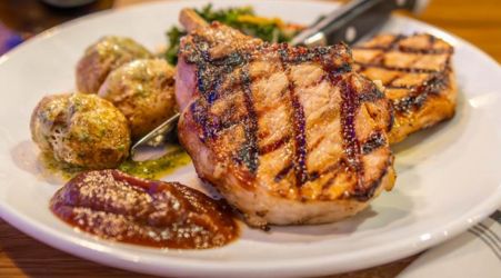 A grilled pork chop with baby potatoes, grilled salmon, and sauce on a white plate.