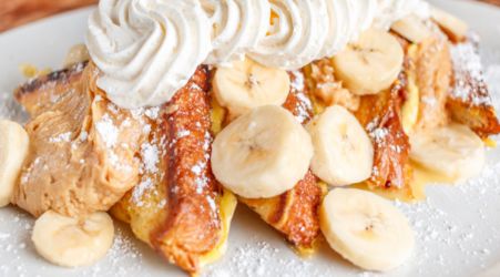 French toast topped with banana slices, whipped cream, and powdered sugar.