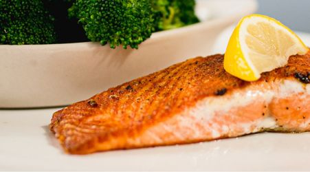 A grilled salmon filet with a lemon wedge next to a bowl of broccoli.
