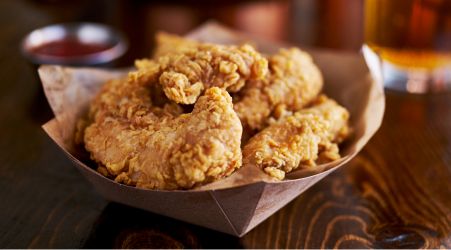 Basket of crispy fried chicken tenders with a side of dipping sauce.