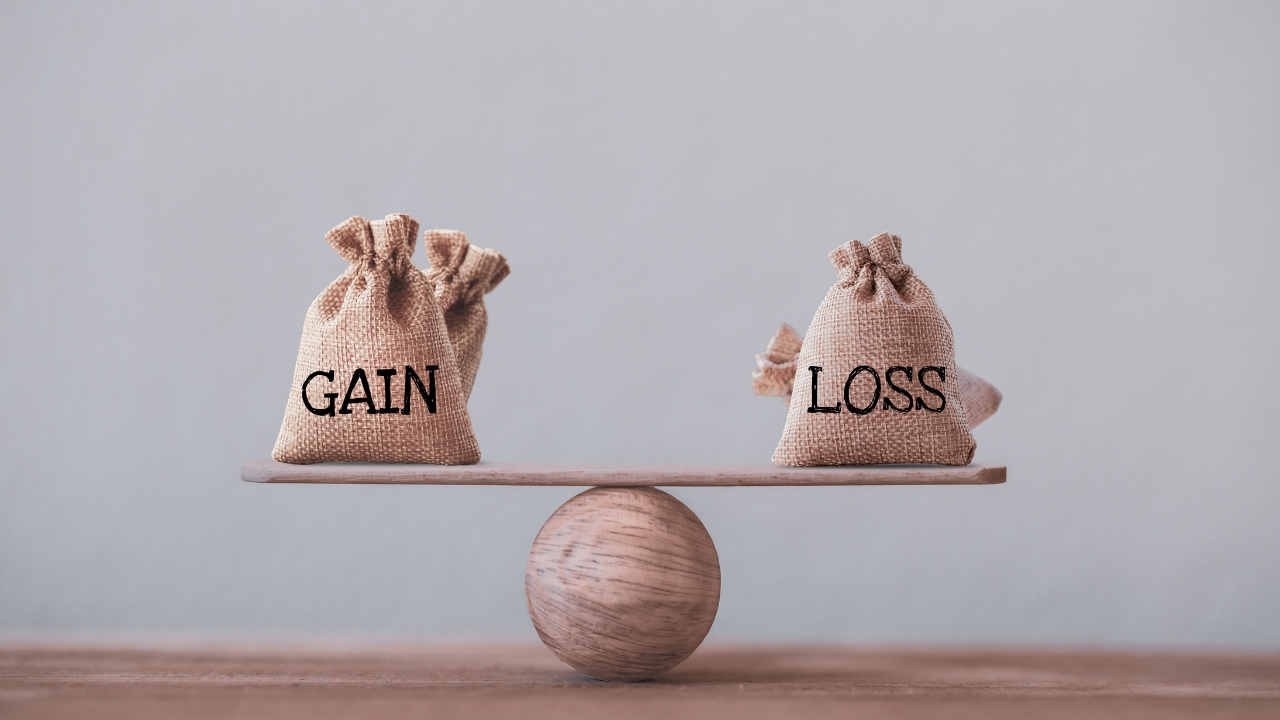 Two burlap sacks labeled "GAIN" and "LOSS" balanced on a wooden seesaw.