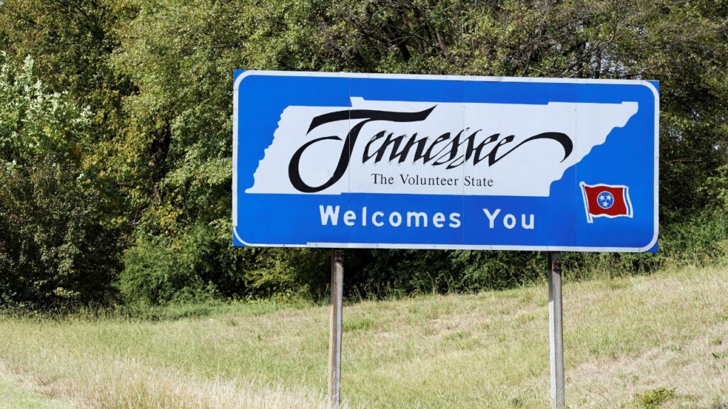 Blue road sign reading "Tennessee Welcomes You" with trees in the background.