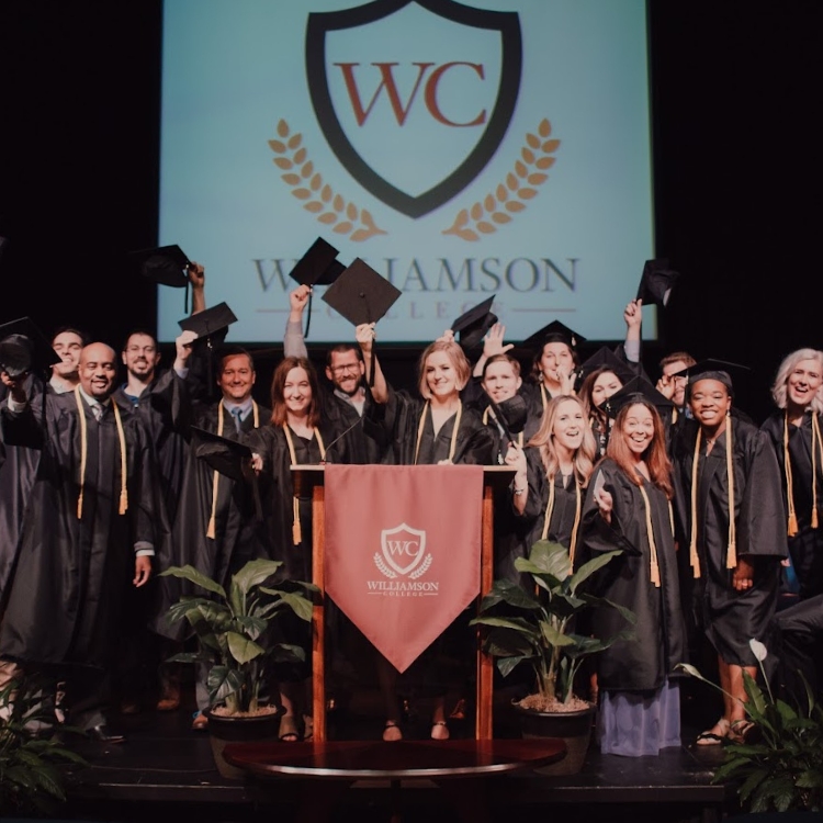 Group of graduates in caps and gowns celebrating on stage at Williamson College.