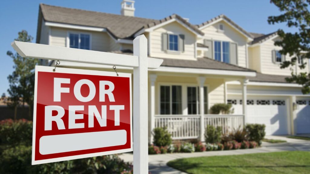 A red "For Rent" sign in front of a house.