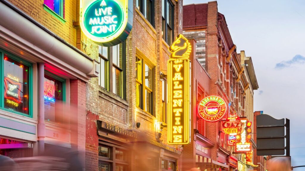 Neon signs for live music venues on a busy street in Nashville.