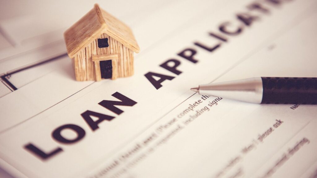 A loan application form with a small wooden house model and a pen.