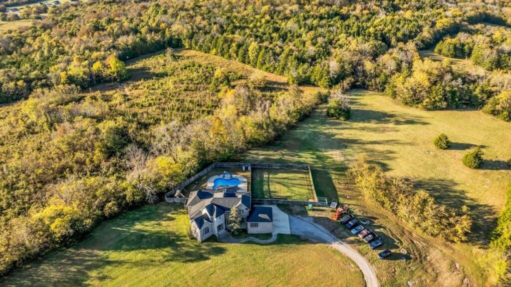 Aerial view of a home with fenced yard surrounded by rolling wooded land in Lebanon, Tennessee.