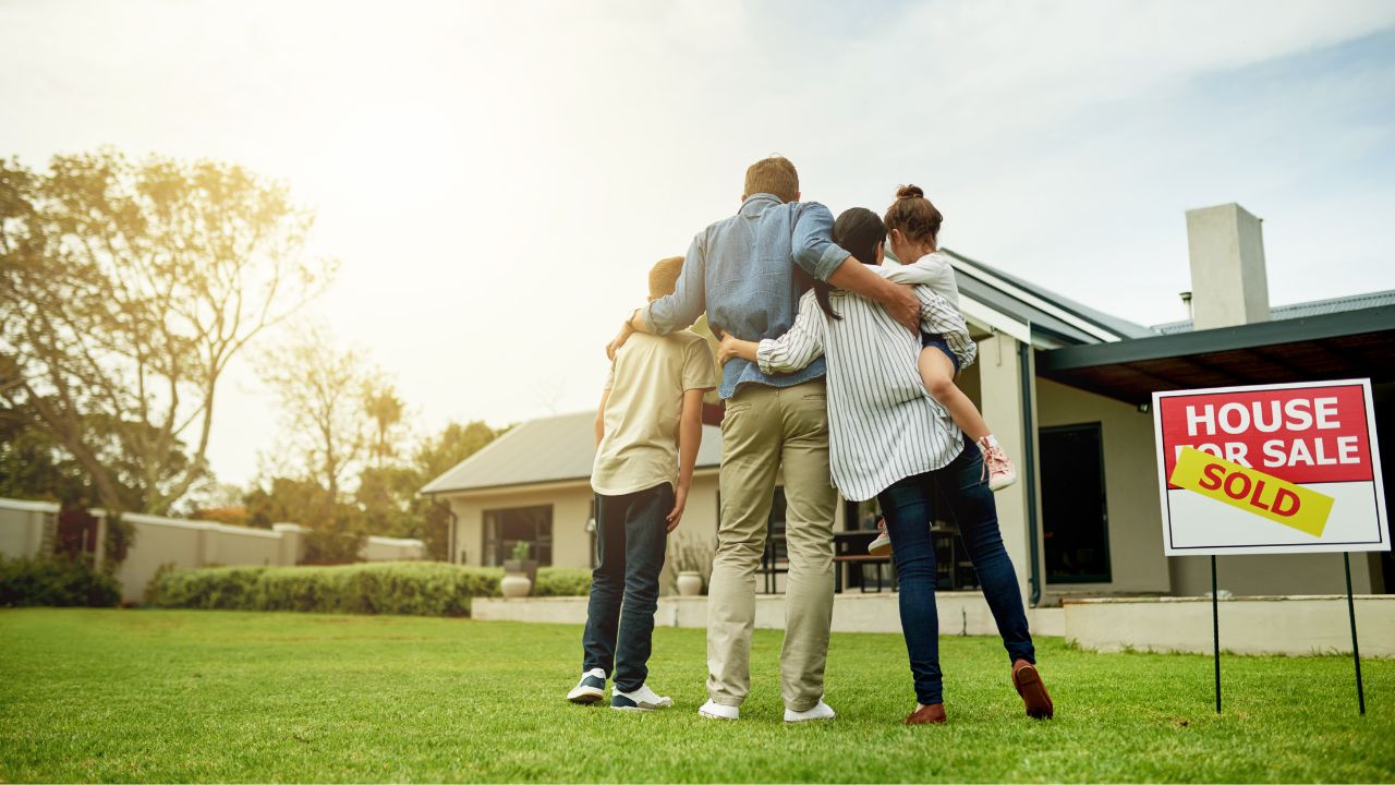 A family stands in front of their home with a sold sign in the yard.