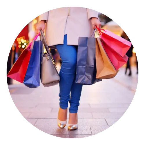 Shopper carrying multiple colorful shopping bags at an outdoor retail center.